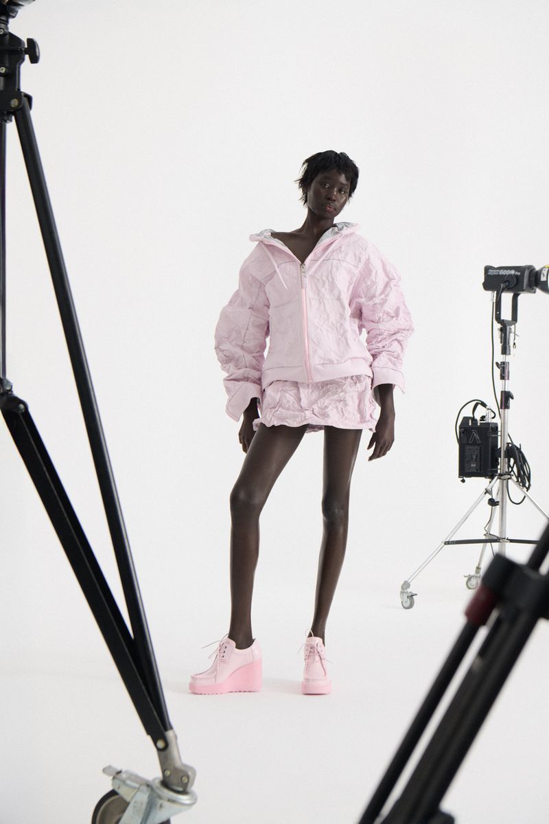 Editorial fashion shot of an African woman posing in pink matching jacket and skirt, with cameras and equipment in a photo studio.