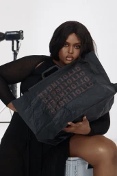 Black woman seated holding a black Ottolinger tote bag against a white studio background.
