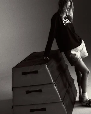 Model Daphne Groeneveld leaning against a gym vaulting box wearing a black Adanola sweatshirt and white shorts in a studio setting.