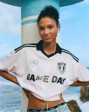 An adult female wears a Hugo-branded sports jersey outdoors near the beach, showcasing a contemporary blend of fashion and athleticism.