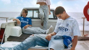 Models relaxing in and around the back of a white pickup truck parked by the ocean for the HUGO SS25 campaign.