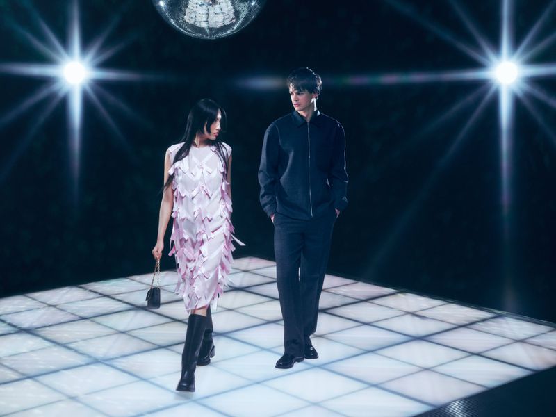 A stylish couple is walking on a disco dance floor in front of a disco ball and bright stage lights, creating a vibrant scene.