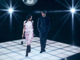 A man and a woman walking on an illuminated stage under bright lights and a disco ball, for a FLANNELS campaign photographed by Scandebergs.