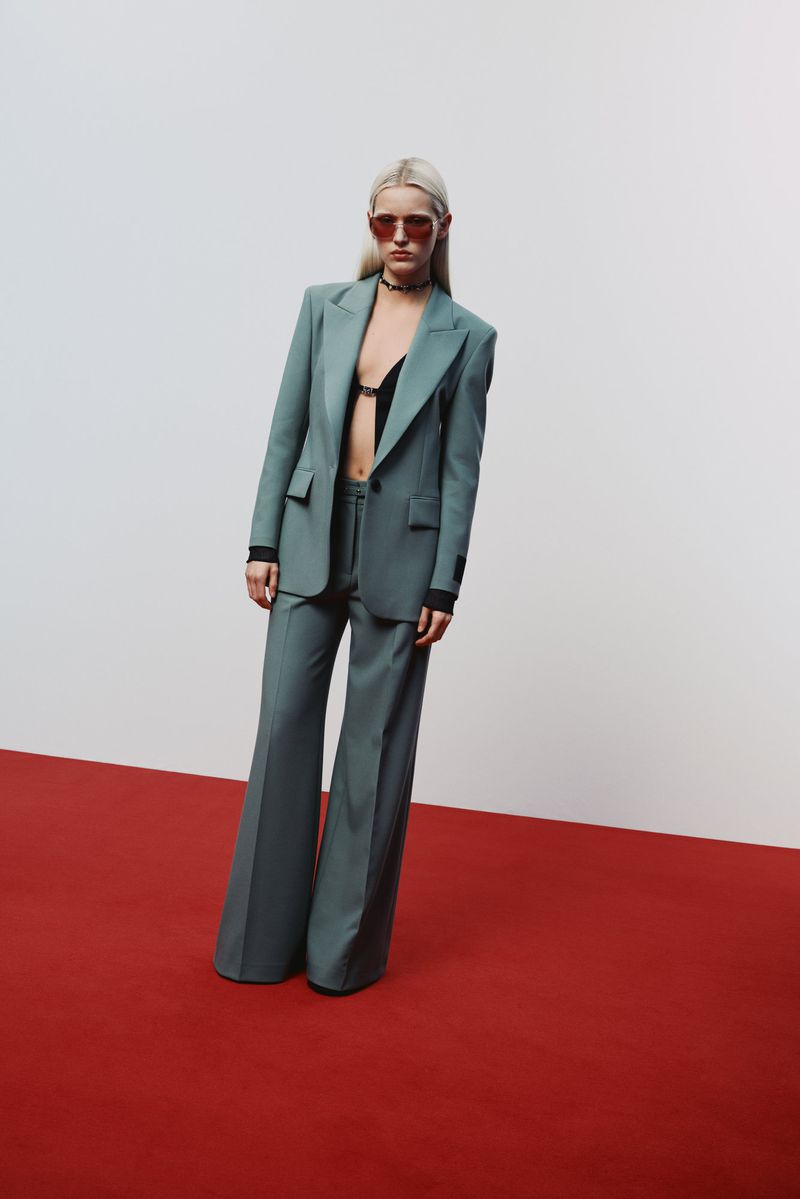 Fashionable woman with blonde hair in blue blazer and pants on red carpet with sunglasses and black top posing in studio for fashion shoot.