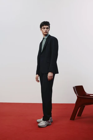 Model in a black suit standing on a red floor against a white background for HUGO Spring 2025 Lookbook