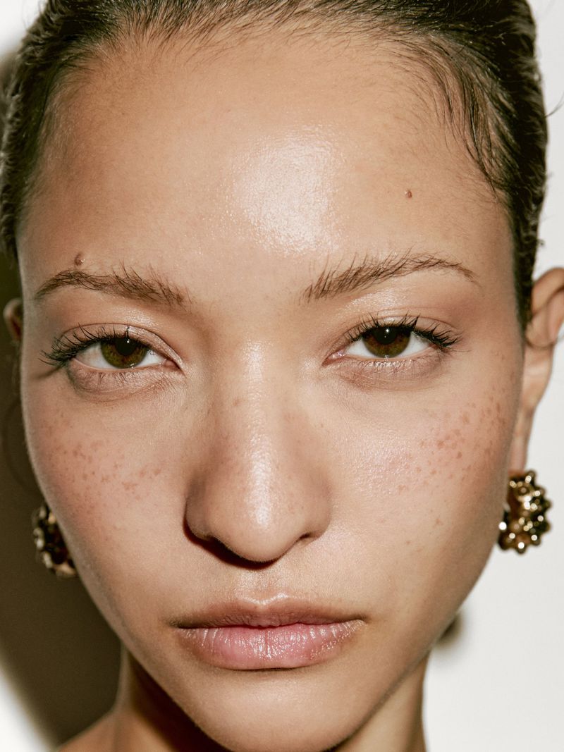 Close-up portrait of a woman with freckles and an earring, featuring a shallow depth of field against a neutral background.