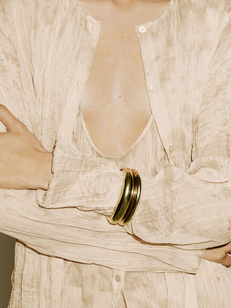 Close-up of a woman in a textured, sheer top with a gold bracelet, showcasing fashion and style with a focus on the bracelet.