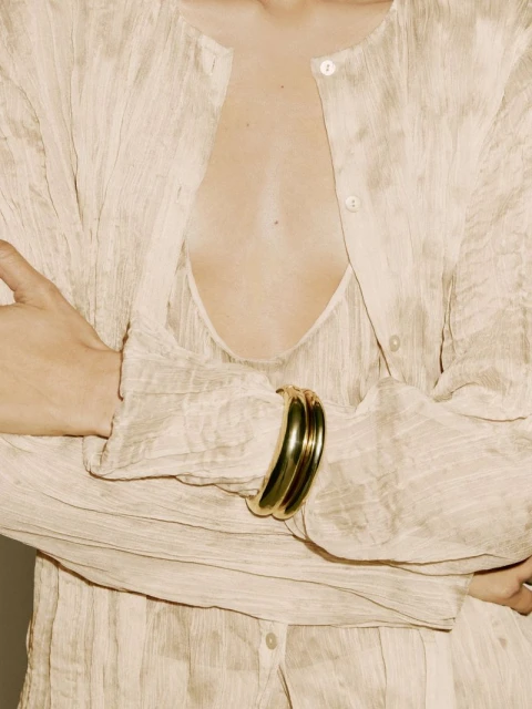 Close-up of a woman in a textured, sheer top with a gold bracelet, showcasing fashion and style with a focus on the bracelet.