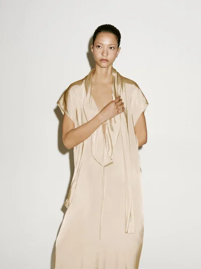 Model wearing a flowing satin dress standing against a plain white background for Massimo Dutti