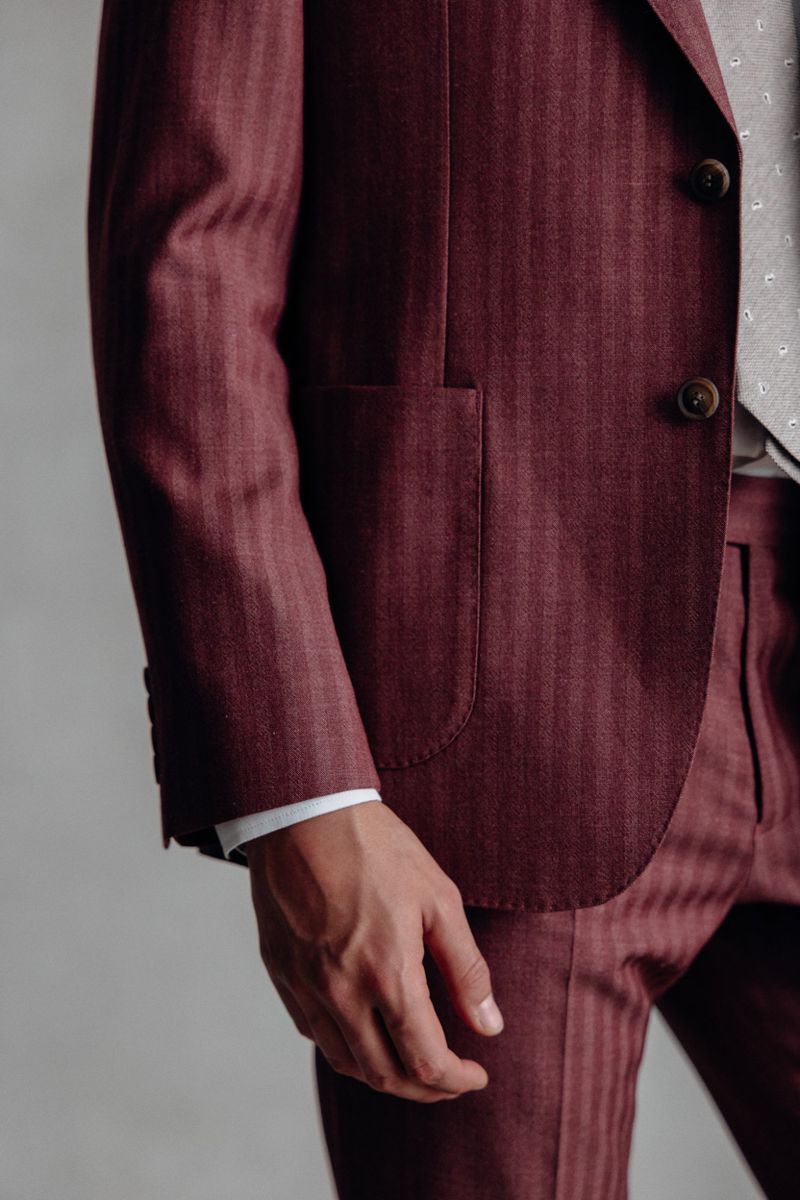 Close-up studio shot of a fair-skinned adult male wearing a maroon pinstripe suit with a vest, the focus is on the suit's texture and fit.