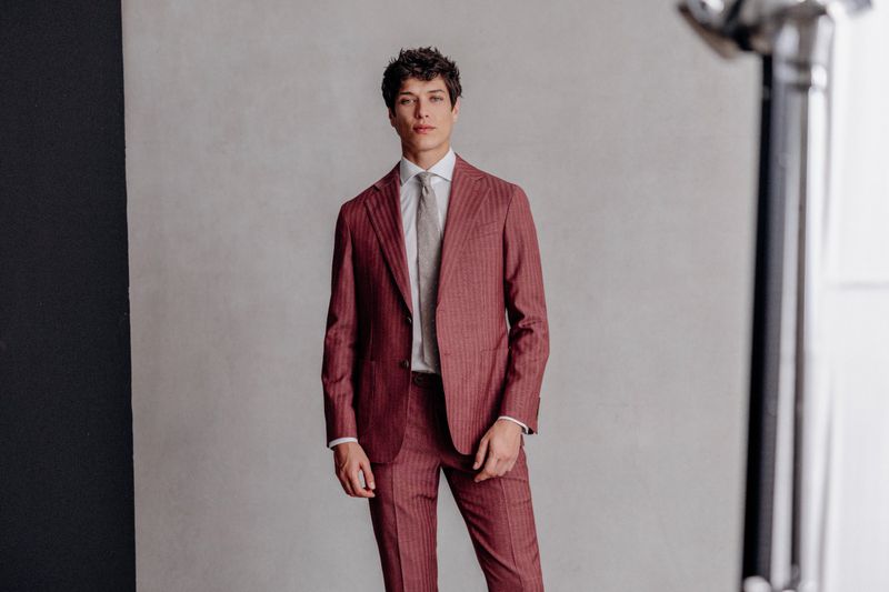 Portrait of adult male in a red pinstripe suit, white shirt, and gray tie standing in a photo studio with lighting equipment.