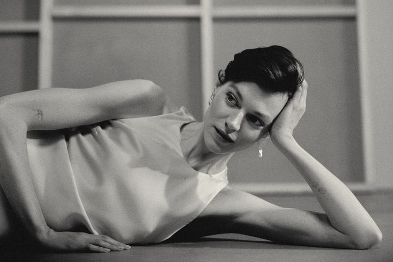 Black and white portrait of an adult female reclining, with short dark hair, wearing a light-colored top, and soft studio lighting.