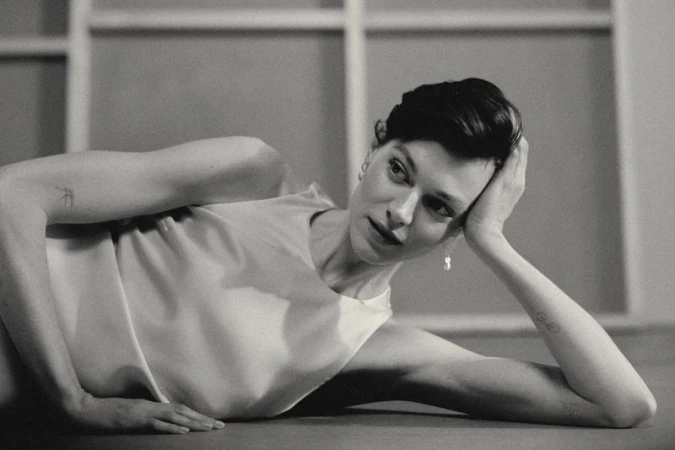 Black and white portrait of an adult female reclining, with short dark hair, wearing a light-colored top, and soft studio lighting.