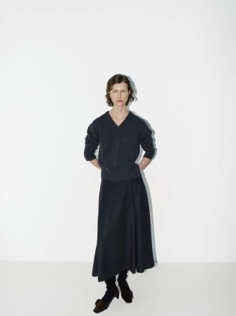 A woman poses in a fashion studio wearing a navy knit sweater and matching long skirt, complemented by dark socks and distinctive heeled shoes.