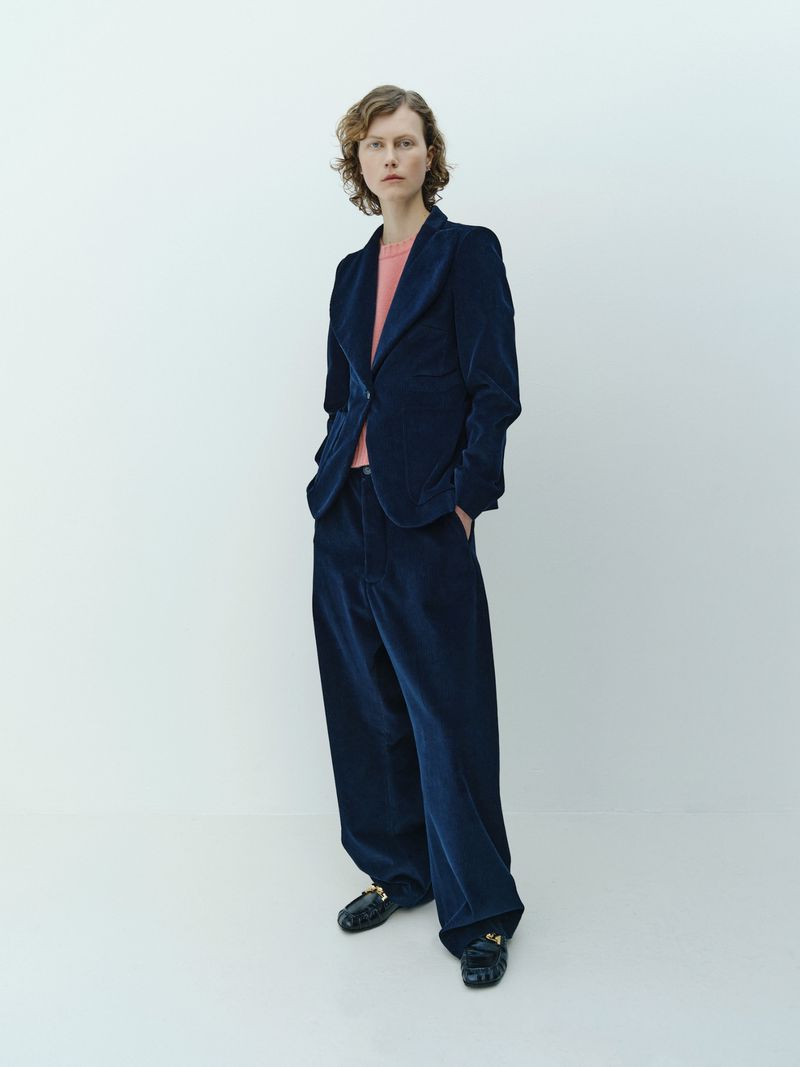 Adult female fashion model poses in a blue corduroy pantsuit with a pink t-shirt in a photo studio with a white background.