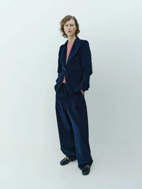 Adult female fashion model poses in a blue corduroy pantsuit with a pink t-shirt in a photo studio with a white background.