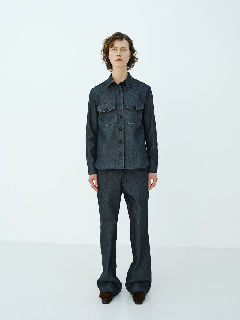 Full-length shot of a young woman in a button-down denim shirt and denim pants in a white studio setting. Fashion photography.