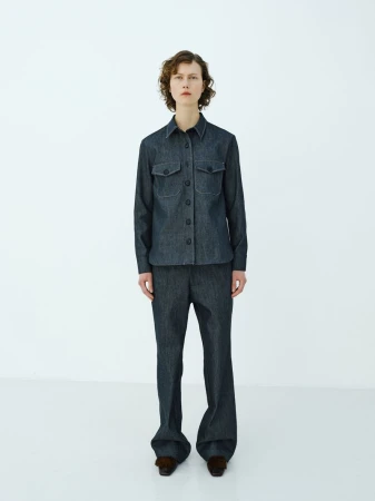 Full-length shot of a young woman in a button-down denim shirt and denim pants in a white studio setting. Fashion photography.