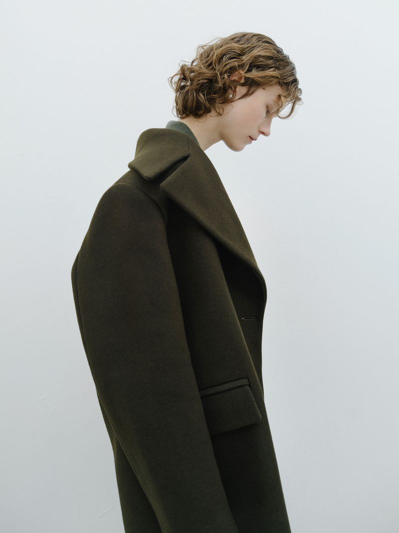 Woman in a green wool coat posing in front of a white background. Fashion studio shot featuring an adult female wearing outerwear.