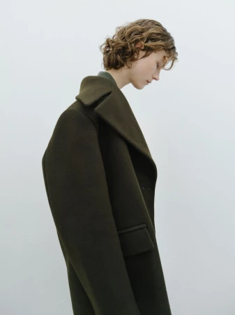 Woman in a green wool coat posing in front of a white background. Fashion studio shot featuring an adult female wearing outerwear.