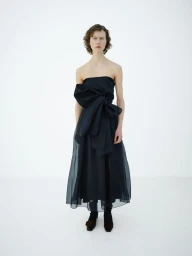 A model wearing a strapless black dress with an oversized front bow against a white studio background.