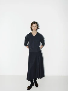 Model standing against a white studio background wearing a dark charcoal v-neck knit sweater and matching flared midi skirt.