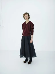 Model wearing a deep burgundy V-neck sweater and a sheer black midi skirt against a clean white studio background.