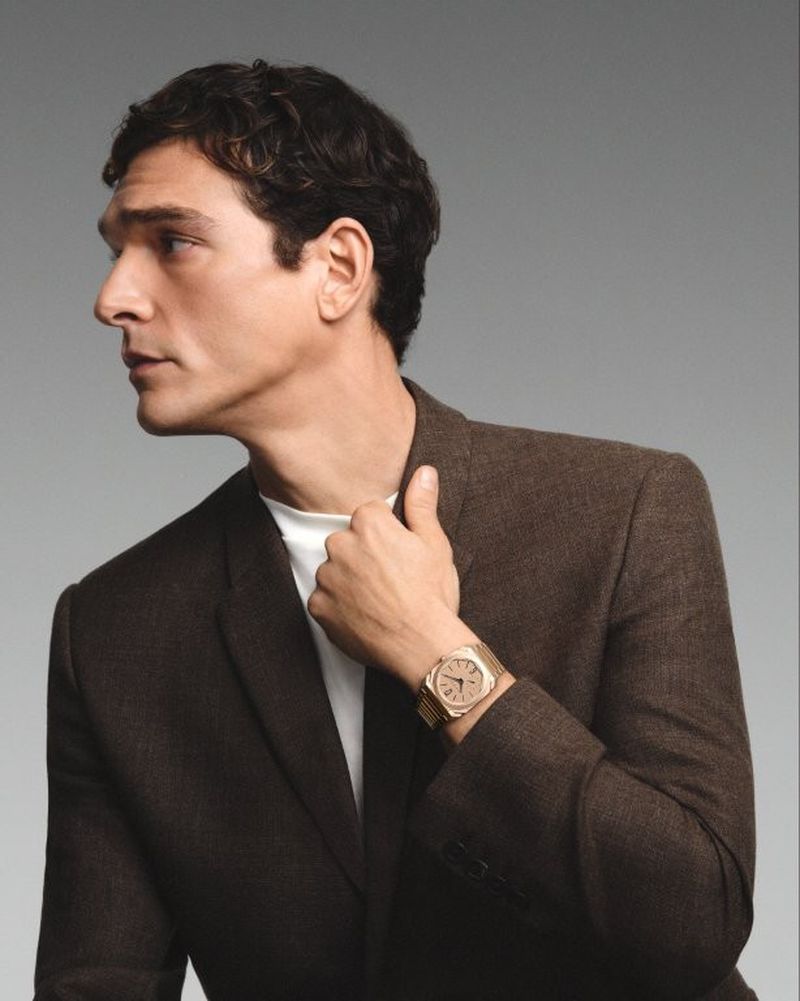 Adult man in a suit, portrait with gold watch. Studio shot of an adult male in a brown suit posing against a grey backdrop.