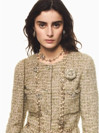 Fashion editorial shot of a woman wearing a Chanel tweed jacket and pearl jewelry, posing in front of a bright neutral backdrop.
