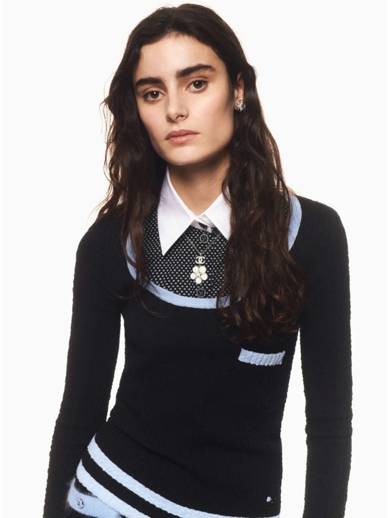 Portrait of an adult female model wearing a black sweater with blue trim and a white collared shirt in a photo studio.