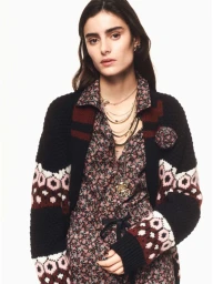 Model wearing a patterned floral shirt and a black knit cardigan with fair isle sleeves against a plain white background