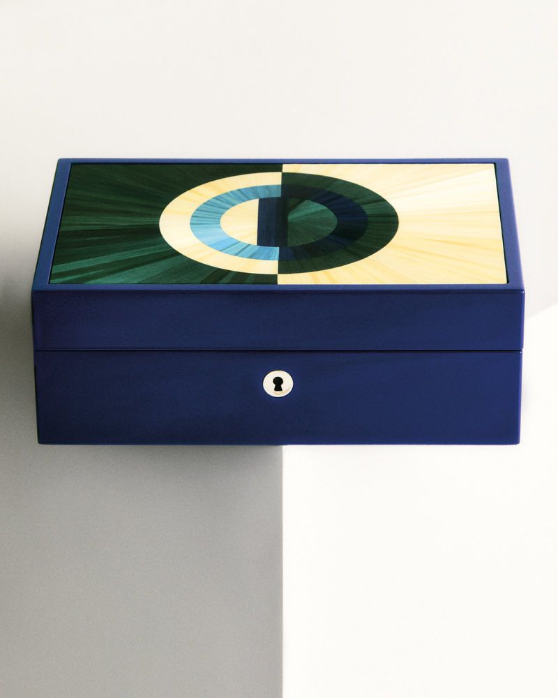 Blue wooden box with geometric marquetry pattern in green, beige, and blue tones on a white surface and grey shadows.