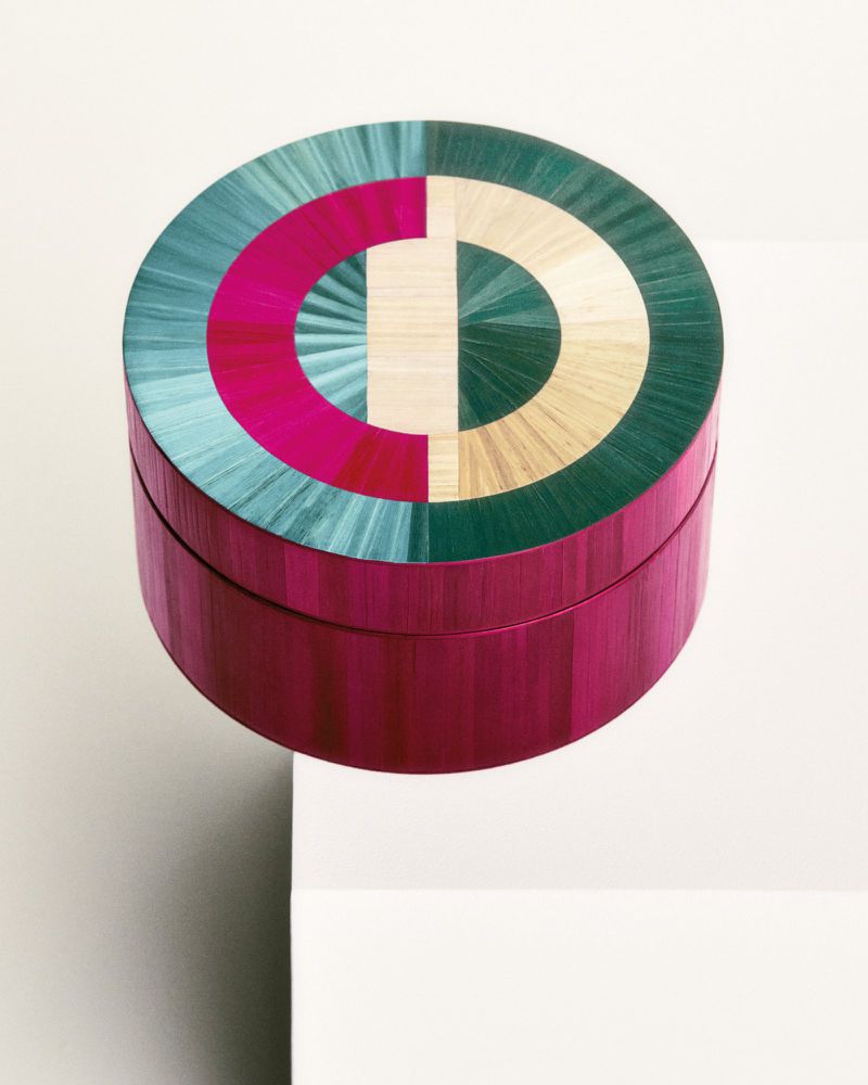 Elevated view of a round container featuring geometric color-blocked design in shades of pink, teal, beige, and green.