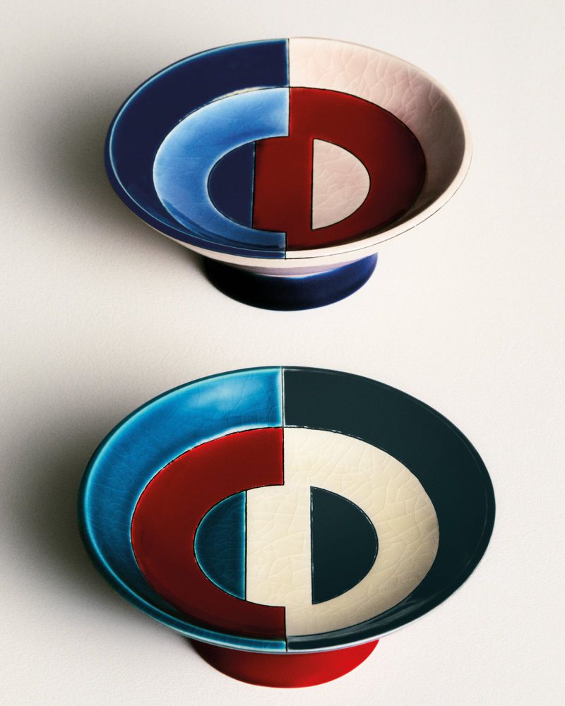 Two colorfully glazed ceramic footed bowls with geometric designs, one navy and pink, the other turquoise and white, on a white surface.