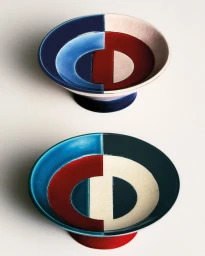 Two ceramic footed bowls with geometric blue, burgundy, and cream glazed monogram patterns on a white surface.