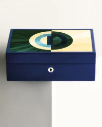 Lacquered royal blue jewelry box with a geometric straw marquetry lid and a silver keyhole on a minimalist backdrop.