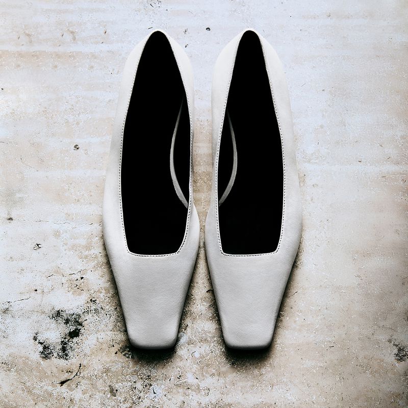 Overhead shot of a pair of white leather square toe pumps on a textured neutral background with subtle discoloration. Simple fashion.