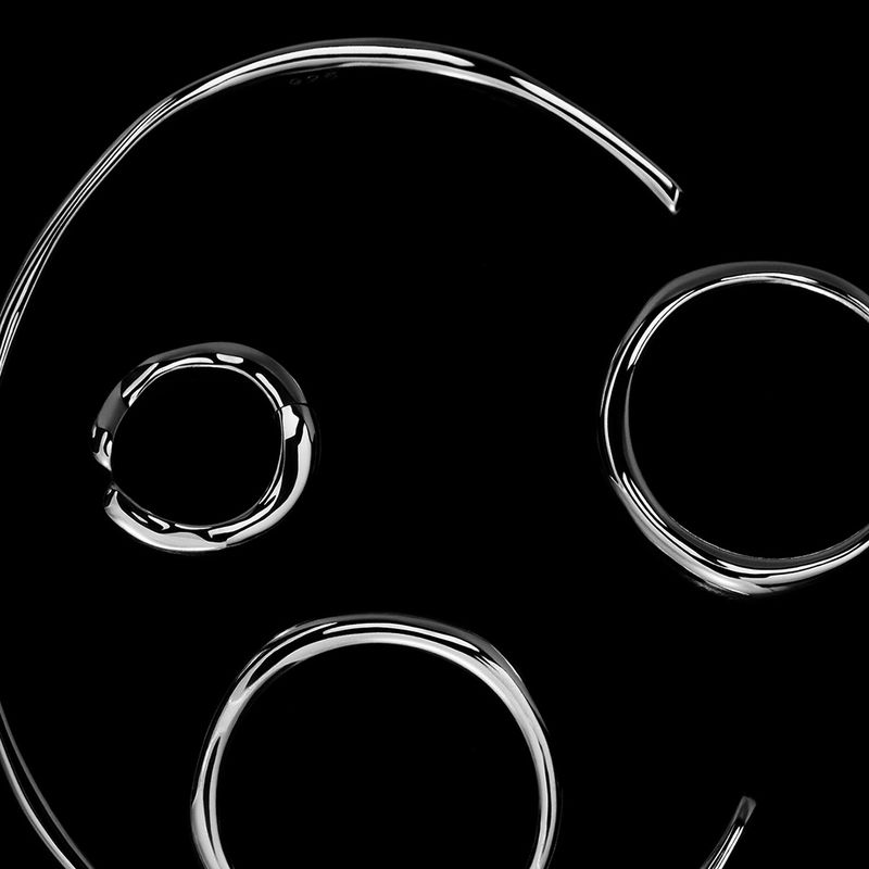 Minimalist still life of chrome metal jewelry, featuring rings and a choker, set against a stark black background with studio lighting.