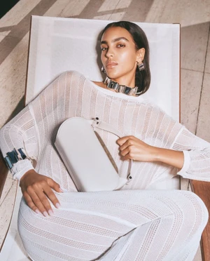 Model reclining in a white knit outfit holding a handbag, for Ferrari Resort 2025 by photographers Bruno and Nico.