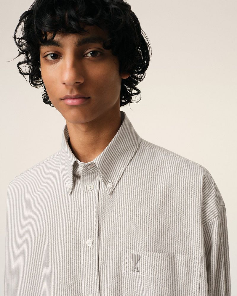 Portrait of a young adult male with dark curly hair wearing a light striped button-down shirt, posing in front of a neutral background.
