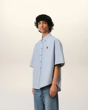 Studio shot of a male model wearing a light blue short-sleeve button-down shirt and jeans, posing against an off-white backdrop.