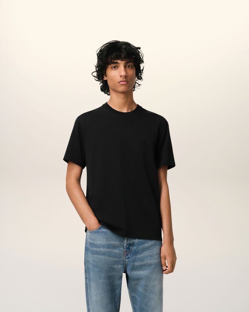 Max Everist wearing a plain black crewneck t-shirt and blue jeans against a neutral studio backdrop.