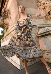 Model Lily Vander Meeden poses in a printed puff-sleeve midi dress beside a carved stone building for Ulla Johnson.