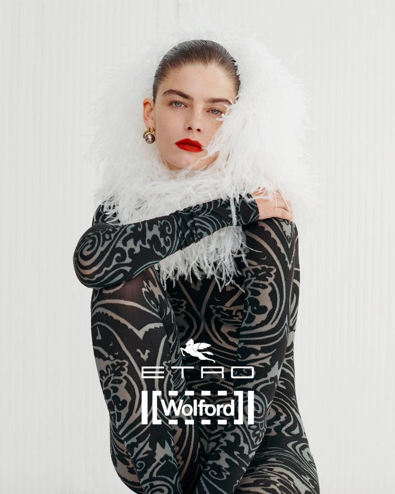 Fashion shot of a woman wearing patterned bodysuit with white feathered collar. Bright red lipstick and hair pulled back, indoor setting.