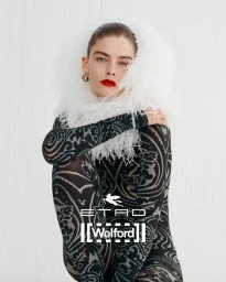 Model wearing a patterned black catsuit with a white feather collar against a seamless white background.