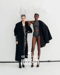Two female models wearing patterned outfits, black coats, and feathered headpieces against a white background