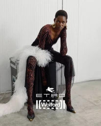 Model Caren Jepkemei seated on a flight case in patterned brown top and tights, draped with white feathers for Etro X Wolford.