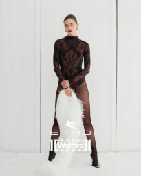 Model in patterned brown bodysuit holding white feather boa against white backdrop