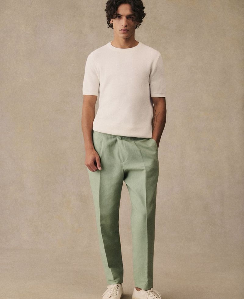 Male model in off-white shirt and light green pants. Studio shot. Fashionable casual wear, neutral background, relaxed pose, modern style.