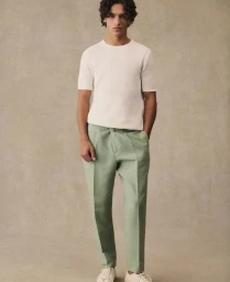 Model wearing a white knit t-shirt and sage green tailored trousers posing against a neutral textured studio backdrop.